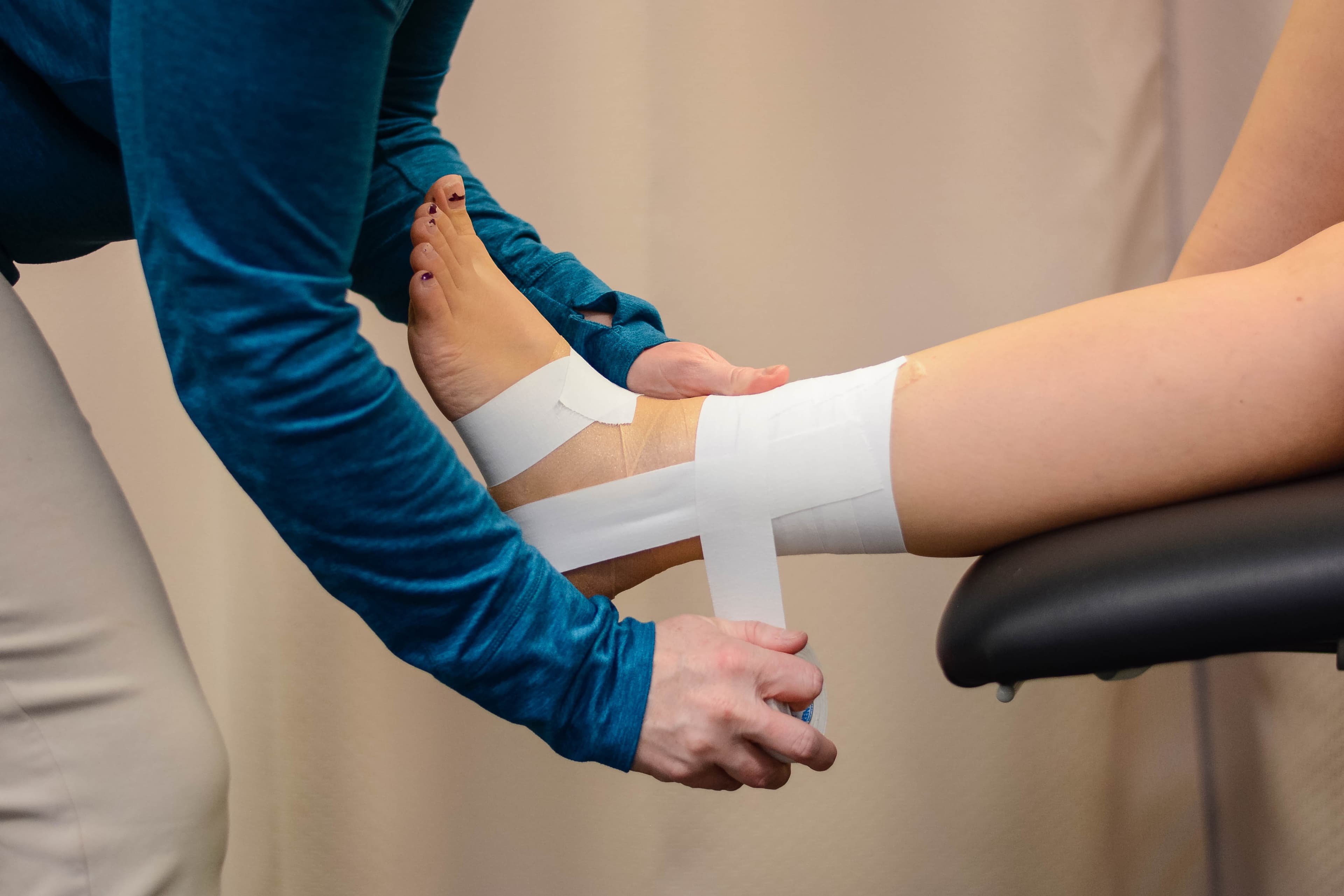 A physio wrapping a patient's ankle in medical tape