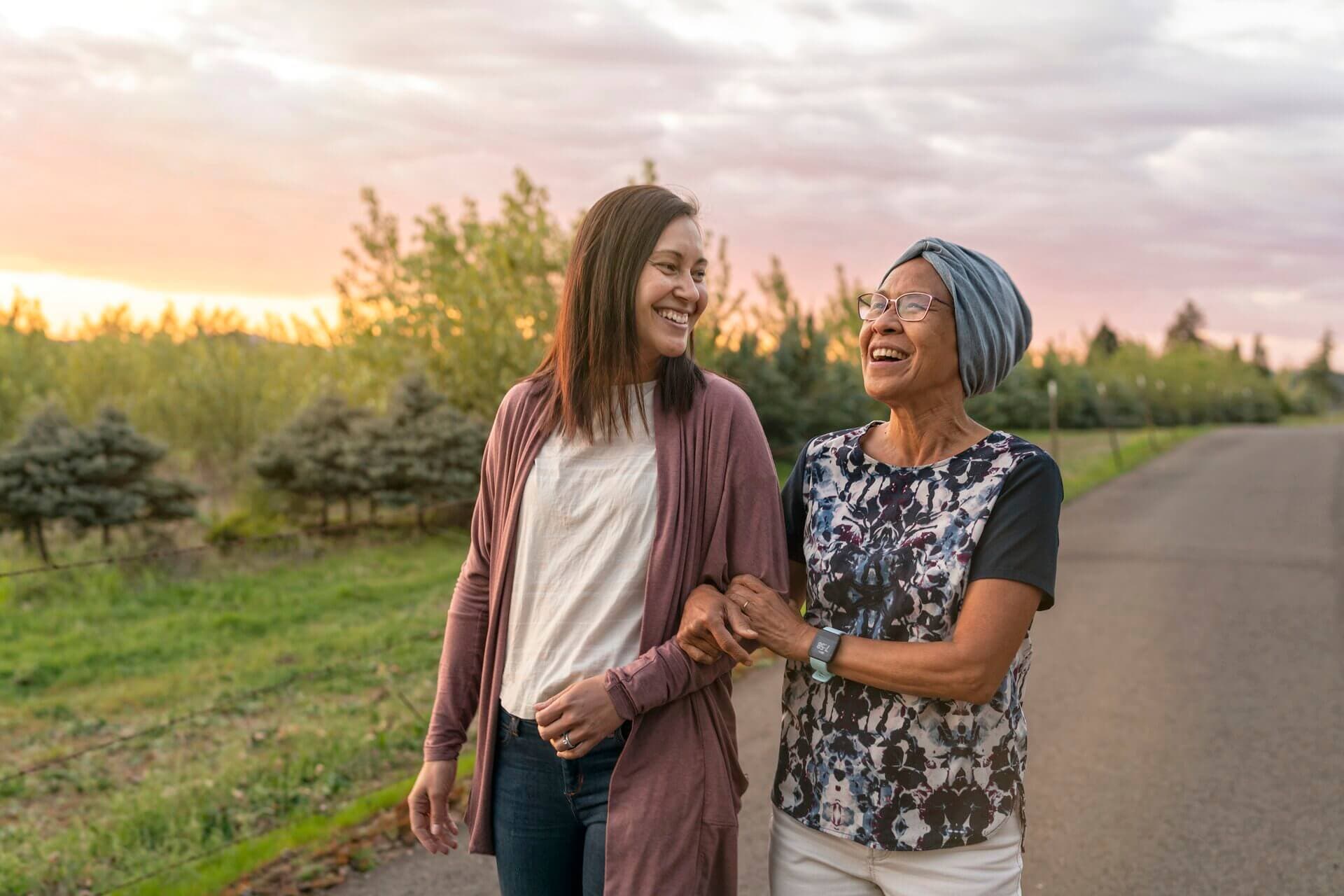 two ladies smiling walking down a path arms linked