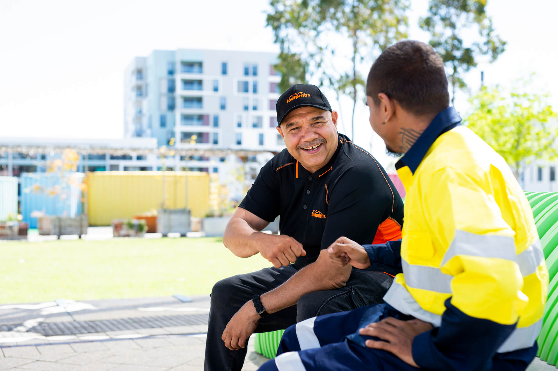 Older man smiles and talks to young worker in high-vis top
